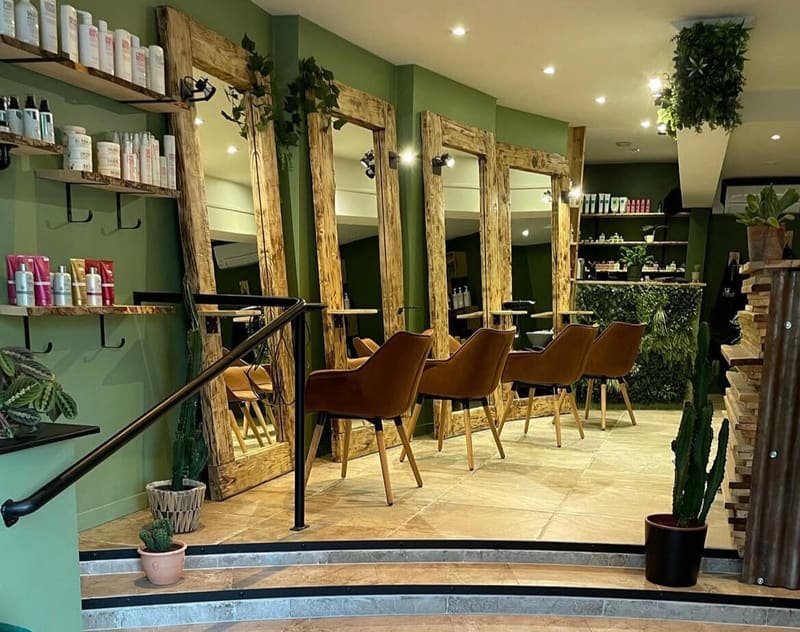 Postes de coiffage du salon La P’tite Brune à Saumur : miroirs à cadre en bois brut, fauteuils cognac et murs verts